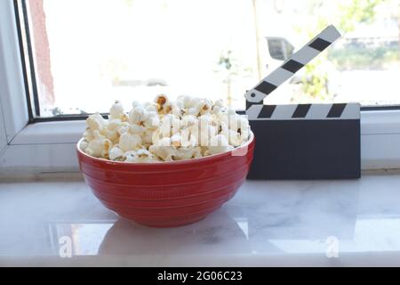 Nahaufnahme einer Schüssel mit Popcorn und Filmklapperboard. Salzige und fetthaltige ungesunde Snacks. Hintergrund in der Unterhaltungsbranche. Stockfoto