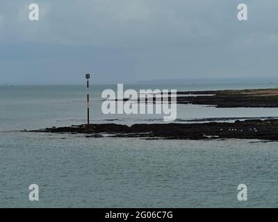 Eine unauffallende Aussicht entlang der Küste von Broadstairs, mit einem sanft gewellten Meer um eine Warnmarke auf einem Felsen, der auftaucht, und entfernten Klippen am Horizont. Stockfoto