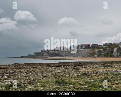 Ein gedämpfter Blick über den Strand von Stone Bay, Kreidefelsen und bunte Strandhütten auf die ferne Landzunge, alles unter einem schweren, drückend bewölkten Himmel. Stockfoto