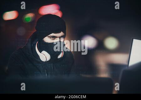 Wütend Computer-Hacker getragen Balaclava stehlen Daten vom Laptop vor schwarzem Hintergrund und blauem Licht. Schließen Porträt. hack-Konzept Stockfoto