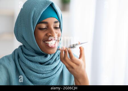 Fröhliche Schwarze Muslimische Frau In Hijab Mit Virtual Voice Assistant Auf Dem Smartphone Stockfoto