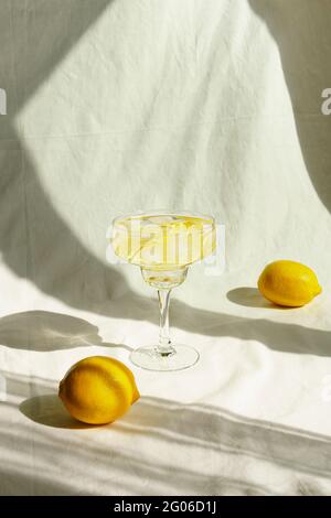 Sommercocktail mit Zitronen und Sonnenschatten. Auf dem Hintergrund aus Leinenstoff. Vorderansicht. Stockfoto