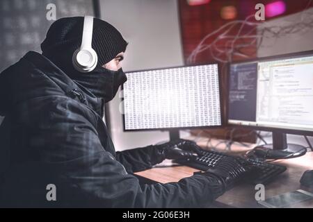 Junge Teenage Hacker Mann mit ihrem Computer, um Malware-Angriff auf globaler Ebene zu organisieren. Sie befindet sich in der geheimen Lage im Untergrund, umgeben von Displays und Stockfoto