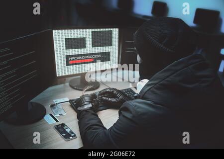 Von der Rückseite zu Hooded Hacker in Corporate Data Server bricht aus seinem unterirdischen Versteck erschossen. Platz hat dunkle Atmosphäre, mehrere Displays Stockfoto