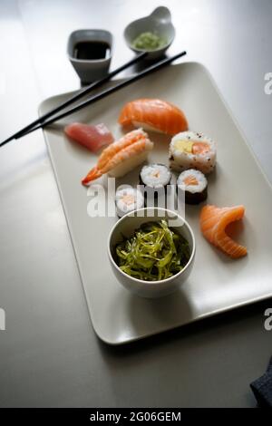 Sushi-Set Nigiri Sashimi und Sushi-Rollen auf Keramikplatte Servierbrett mit Sojasauce, Wasabi, einer Schüssel mit Wakame-Algen und Essstäbchen über Metall-Bac Stockfoto