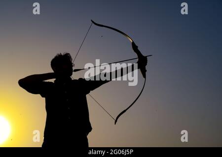 Ein Mann mit Silhouetten, der einen Pfeil und einen Bogen vor einem Sonnenuntergang hält. Stockfoto