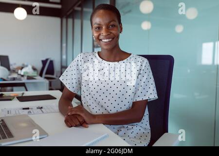 Lächelnde afroamerikanische Geschäftsfrau, die bei der Arbeit am Schreibtisch sitzt Stockfoto