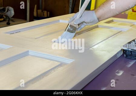 Hand des Reparaturmannes Maler mit Handschuhen mit Farben hölzerne Haustür mit Pinsel in einem neuen Haus Stockfoto