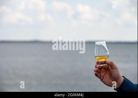 Hand hält einen Schluck Single Malt Scotch Whisky an der Küste In Schottland Stockfoto
