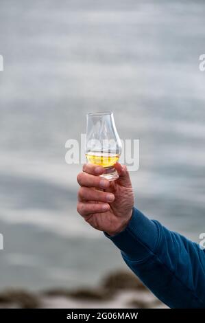 Hand hält einen Schluck Single Malt Scotch Whisky an der Küste In Schottland Stockfoto