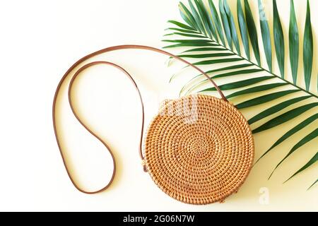 Trendige runde Rattan-Strohtasche und tropische Palmenblätter von oben Stockfoto