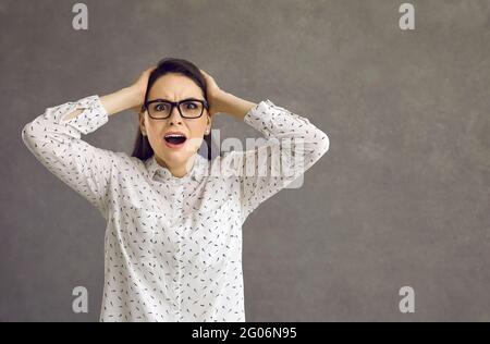 Junge Frau hält den Kopf und fühlt sich in Panik versetzt und steht auf grauem Hintergrund Stockfoto