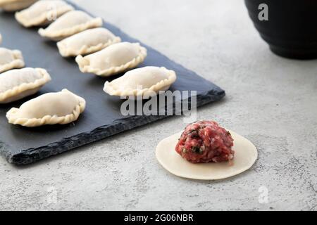 Die fertigen Knödel werden auf einem schwarzen Schiefersteinbrett in einer Reihe gelegt. Stockfoto