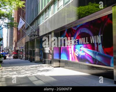 „Wissenschaft wird gewinnen“-Slogan im Fenster der Pfizer-Hauptniederlassungen in der 235 E 42nd Street, New York, NY, mit Pfizer-Flagge und Menschen in der Ferne auf dem Bürgersteig in NYC, während die Vereinigten Staaten Fortschritte bei der Covid-Impfung machen. Stockfoto