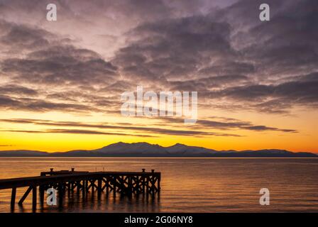 Ein wunderschöner Sonnenuntergang hinter der Isle of Arran, aufgenommen vom alten Pier in Portencross in North Ayrshire, Schottland. Stockfoto