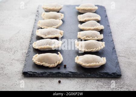 Die rohen Knödel werden auf einem schwarzen Schiefersteinbrett in einer Reihe gelegt. Stockfoto