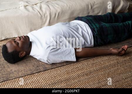 Yoga. Afrikanischer junger Mann, der auf einem Boden meditiert und in Shavasana-Pose liegt. Stockfoto