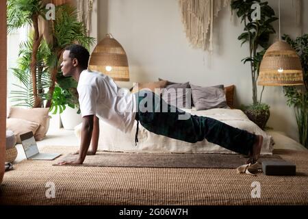 Afrikanischer Mann, der zu Hause Yoga in Plankenpose praktiziert Stockfoto