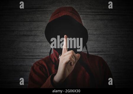 Eine unbekannte Person ohne Gesicht in einer Kapuze zeigt eine Fingerbewegung, die Städte bedeutet. Das Konzept der Anonymität und Geheimhaltung im Netzwerk. Stockfoto