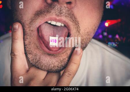 Nahaufnahme eines jungen Junkie-Mannes, der LSD nimmt. Guy Swallows legt vor dem Hintergrund eines Konzerts in einem Club eine Art Betäubungsmittel auf seine Zunge. Junkie Stockfoto