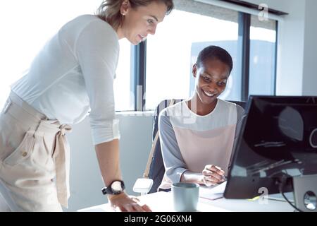 Zwei lächelnde Geschäftsfrauen arbeiten zusammen, nutzen Laptops und sprechen Stockfoto