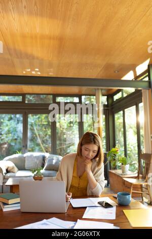 Asiatische Frau mit Laptop und Schreiben, arbeiten von zu Hause aus Stockfoto