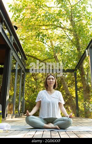 Asiatische Frau praktiziert Yoga auf der Terrasse im Garten Stockfoto