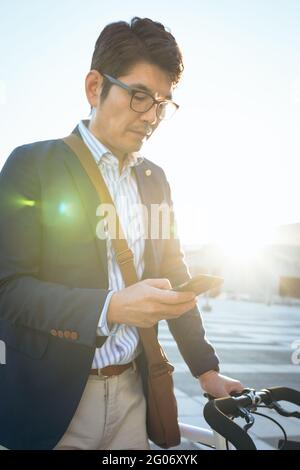 Mittelteil des asiatischen Geschäftsmannes mit Smartphone hält Fahrrad in der Stadt Straße Stockfoto