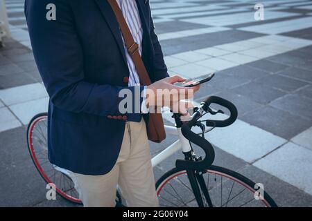 Mittelteil des asiatischen Geschäftsmannes mit Smartphone hält Fahrrad in der Stadt Straße Stockfoto