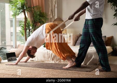 Yoga-Lehrer oder Pilates-Ausbilder helfen jungen Mann, Muskeln zu strecken tun nach unten schauenden Hund Stockfoto