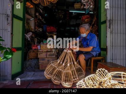 Ein älterer männlicher Arbeiter bündelt vor der Vorderseite seines Ladens in der Chinatown-Gegend von Bangkok, Thailand, einige aus Bambus hergestellte Produkte Stockfoto