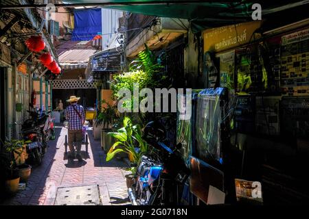 Ein männlicher Straßenverkäufer schiebt seinen Wagen entlang einer sonnenbeschienenen Gasse in der Chinatown-Gegend von Bangkok, Thailand Stockfoto