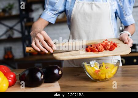 Teilansicht einer jungen erwachsenen Frau, die in der modernen Küche in Scheiben geschnittene Kirschtomaten in Gemüsesalat gab Stockfoto