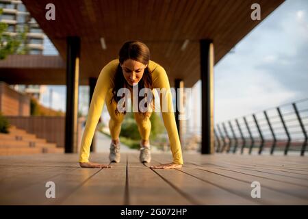 Hübsche junge Frau, die Liegestütze auf einem Holzsteg bei der aufführt Fluss Stockfoto