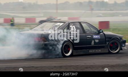 Der Rauch, der während der Veranstaltung unter den Rädern eines grauen Sportwagens zu sehen ist.Festival Drift Expo Track Mode läuft am 29-30. Mai auf dem ADM Raceway mit der Ausstellung von Projekten, die für das Driften modifiziert wurden, wie: ‘Drift Taxi’ - eine Möglichkeit, als Passagier mit einem professionellen Fahrer in einem speziell präparierten Sportwagen auf der Rennstrecke zu fahren, ‘Drift Trike Area’ - eine Plattform, auf der Sie versuchen können, ein echtes Drift Trike zu fahren und ‘RC Drift’ - Drift auf ferngesteuerten Autos. Stockfoto