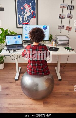 Rückansicht einer Telearbeiterin, die auf einem Fitball sitzt Vor ihrem Schreibtisch Stockfoto