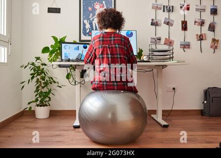 Rückansicht einer Telearbeiterin, die auf einem Fitball sitzt Vor ihrem Schreibtisch Stockfoto