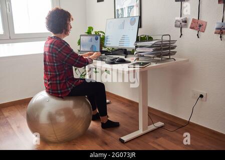 Frau mit Telearbeit sitzt auf einem Fitball vor ihrem Schreibtisch Stockfoto