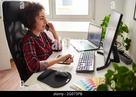 Die junge Designerin verwendet einen digitalen Stift, während sie von zu Hause aus telecommuting und mit Kunden telefoniert Stockfoto
