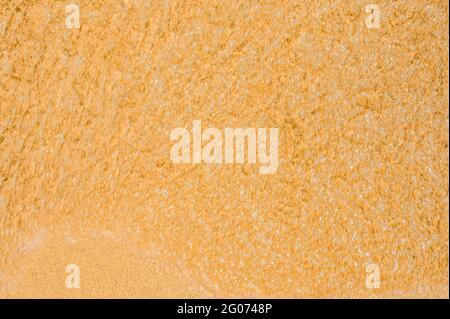 Textur aus nassem Sand am Strand. Sommer Strand Hintergrund. Klares Meerwasser auf goldenem Sand am Strand Stockfoto