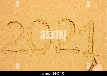 Handgeschriebener Text 2021 auf goldenem nassem Sand am Strand. Erholung nach covid-19 Konzept und Glücksreise Stockfoto