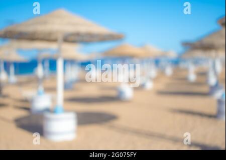 Verschwommenes blaues Meer und weißer Sandstrand mit Sonnenschirm, Liegestuhl. Verschwommener Sonnenschirm Hintergrund. Abstraktes Bokeh Sommer und Meer Hintergrund. Urlaub, Stockfoto