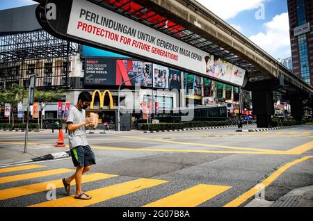 Kuala Lumpur, Malaysia. Juni 2021. Ein Mann, der als Vorsichtsmaßnahme gegen die Ausbreitung des Coronavirus (Covid-19) eine Gesichtsmaske trägt, überquert eine leere Straße. Die malaysische Regierung hat vom 1. Bis zum 14. Juni erneut eine landesweite totale Sperre verhängt, da die Fälle des Coronavirus (Covid-19) in dem Land wie in den letzten Wochen ansteigen. Einkaufszentren und die meisten Geschäftsbereiche sind geschlossen, um die Ausbreitung der Covid-19-Pandemie einzudämmen. Kredit: SOPA Images Limited/Alamy Live Nachrichten Stockfoto