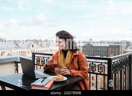 Junge Frau, die mit einem Laptop am Tisch sitzt und im Café im Freien Tee trinkt Stockfoto