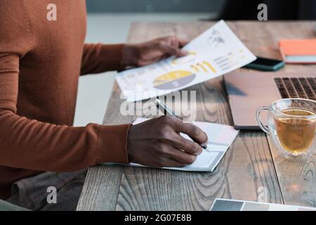 Nahaufnahme eines afrikanischen Mannes, der am Tisch sitzt und mit Geschäftsdokumenten arbeitet Stockfoto
