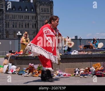 Ottawa, Kanada. Juni 2021. Mitglieder der First Nations-Gemeinschaften veranstalten eine Zeremonie zum Gedenken an die 215 Kinder, die in einer ehemaligen Wohnschule in einer Gedenkstätte vor dem kanadischen Parlament begraben gefunden wurden. Die gebürtige Frau spielt einen zeremoniellen Tanz um die improvisierten Tribut, die versammelt wurden. Quelle: Meanderingemu/Alamy Live News Stockfoto