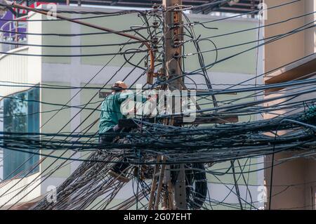 Ein Kommunikationsingenieur, der zwischen einem Kabelgewirr an einem Telegrafenmast in Bangkok in Thailand arbeitet. Stockfoto