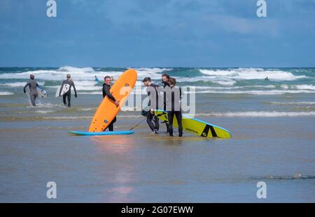 Eine Gruppe von Freunden, die ihre gemieteten Surfbretter tragen und im Meer bei Mawgan Porth auf einem Surfurlaub in Cornish in Großbritannien stehen. Stockfoto