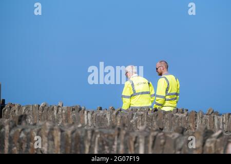 Zwei Cormac-Arbeiter tragen fluureszend gelbe Hi-viz-Sicherheitsjacken, die vor einem strahlend blauen Himmel gesehen werden. Stockfoto