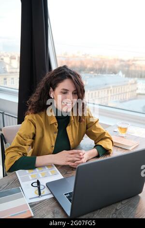 Lächelnde junge Frau in Kopfhörern, die im Büro mit einem Laptop online kommunizieren kann Stockfoto